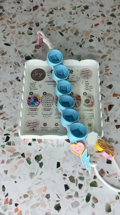 A finished blue clicker keyring resting on the branded Joy Craft card