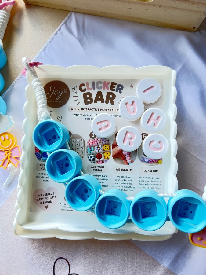 Tray of chunky 3D-printed letter beads beside assembled clickers