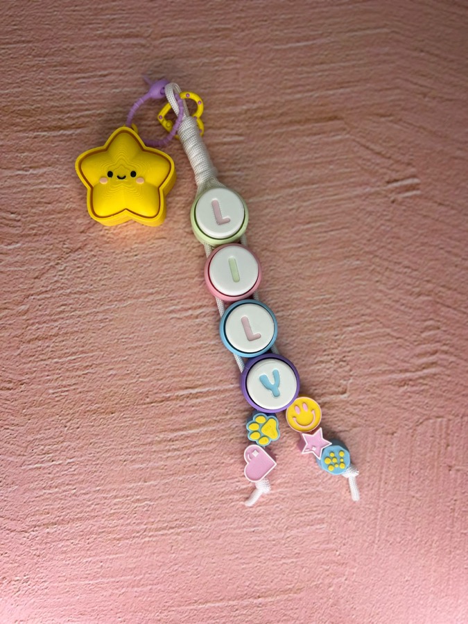 A finished clicker keyring spelling LILY on a white braided cord with a yellow star and charms